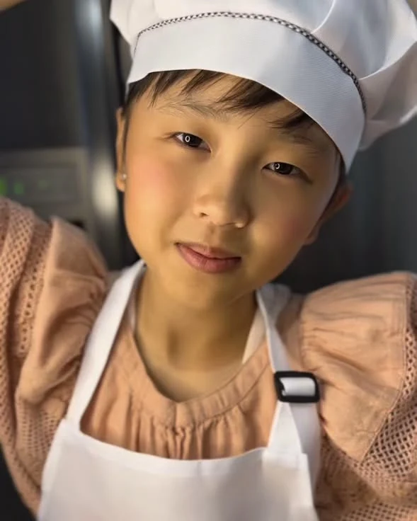 The baker behind KloPoKitchen, in a chef's hat and apron in the kitchen